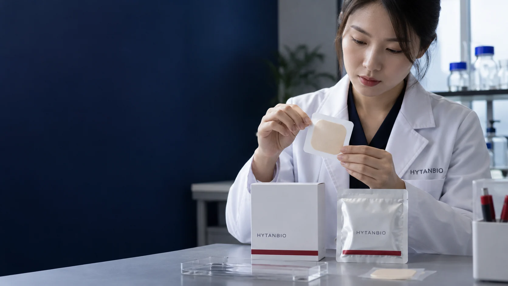 A flat patch prototype and sealed silver sachet next to a neutral white packaging carton — illustrative development scene