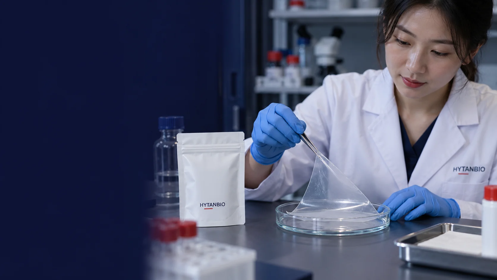 A thin translucent film on a glass dish and separate white pouch sample container on a development tabletop — illustrative development scene
