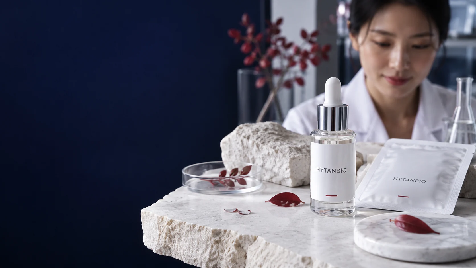 A glass cosmetic serum dropper bottle stands upright next to a flat patch sachet on matte white stone — illustrative development scene
