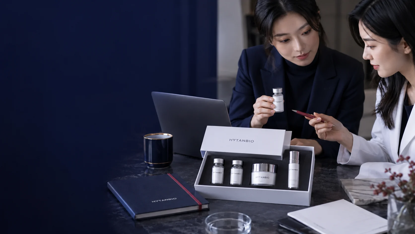 A restrained cosmetic packaging and document desk scene with a laptop and sealed sample set — illustrative development scene