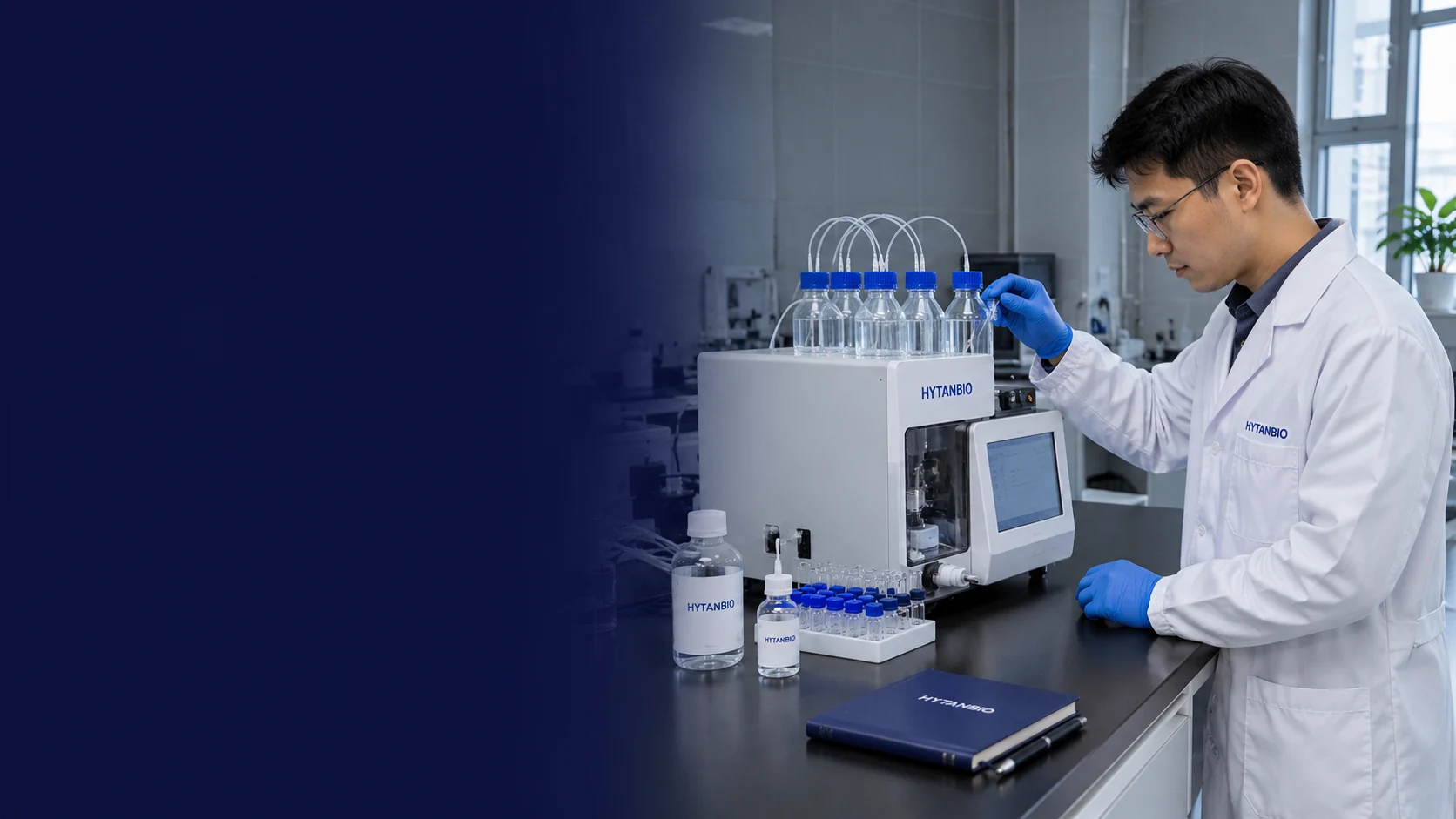 An East Asian male scientist beside a compact peptide synthesis instrument with straight reagent bottles and a dark blue notebook; a different laboratory with gray tiled walls and side window — illustrative development scene