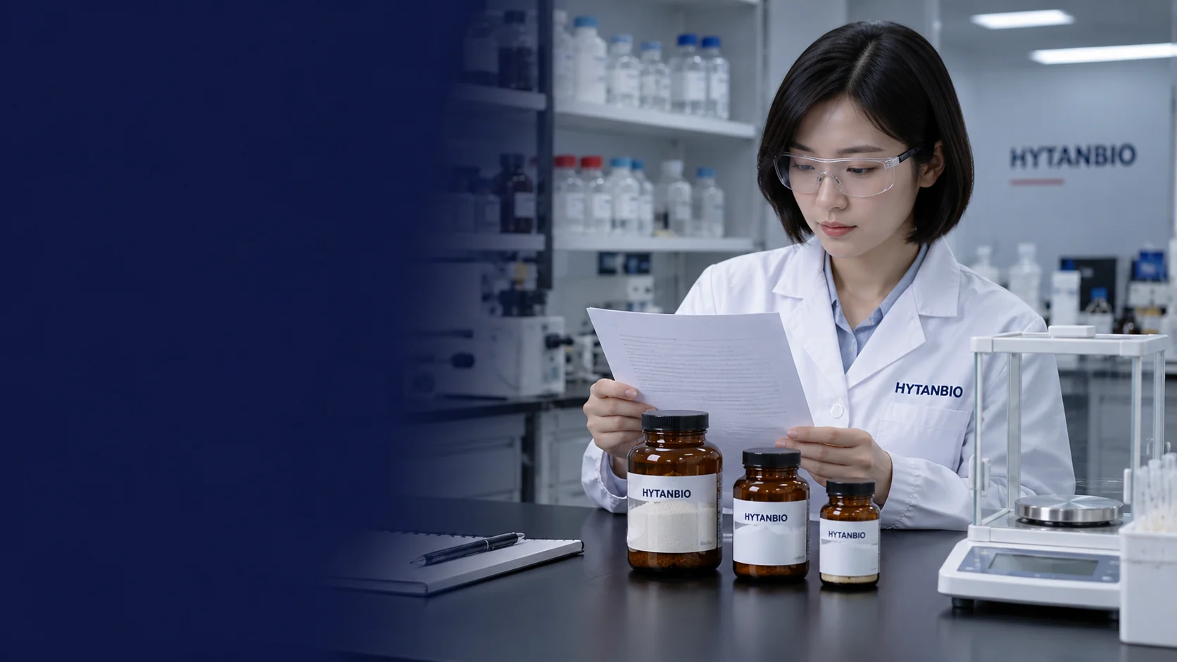 A random East Asian female researcher with short black bob and safety glasses looking at a blank document beside amber powder jars and a clean laboratory balance; no vial in her hands — illustrative development scene