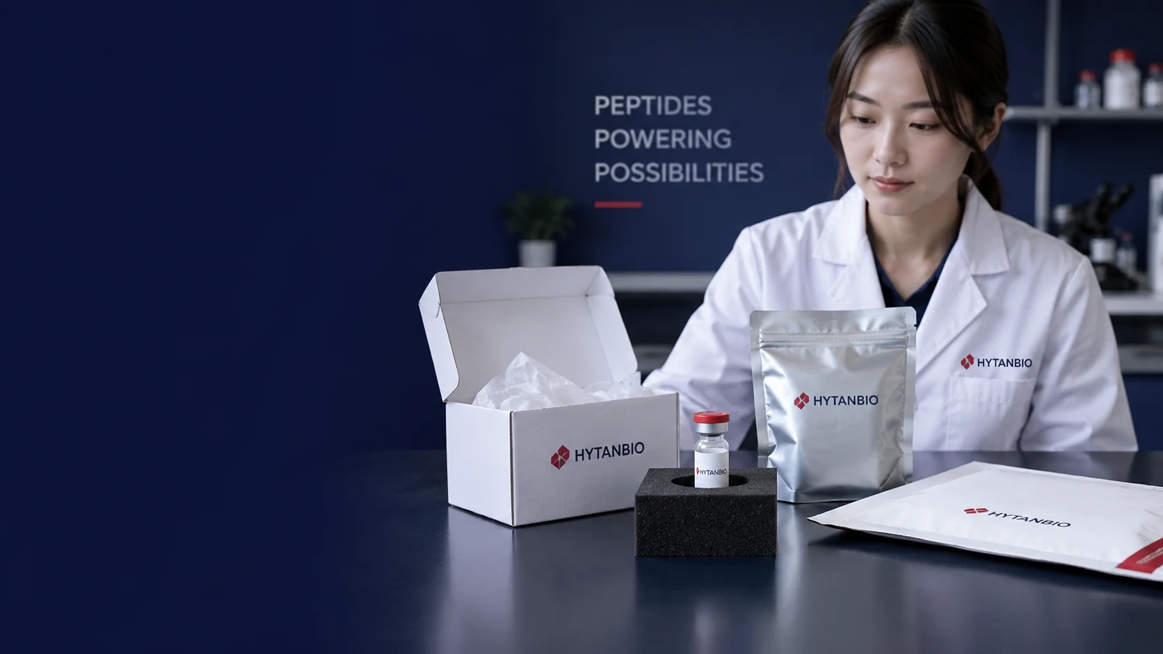 A upright single closed sample vial held securely in a tabletop foam block beside an open white supply carton, packing tissue, closed thermal pouch and a simple plain shipping folder; no hands — illustrative development scene