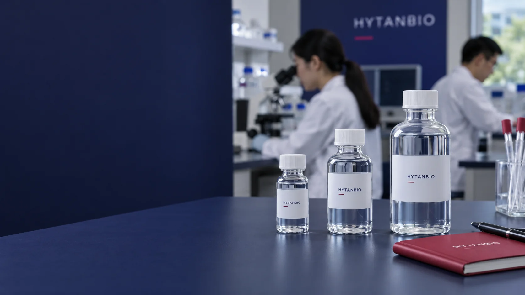 Three perfectly straight closed clear laboratory water vials of different capacities with neutral small HYTANBIO labels on a matte navy stage, small berry notebook and a blurred clean laboratory background — illustrative development scene