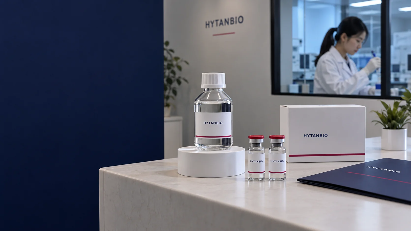Single capped clear solution bottle on a white cylindrical riser next to two smaller upright sealed vials, empty clean carton and navy folder; a warm gray wall and distant lab window — illustrative development scene