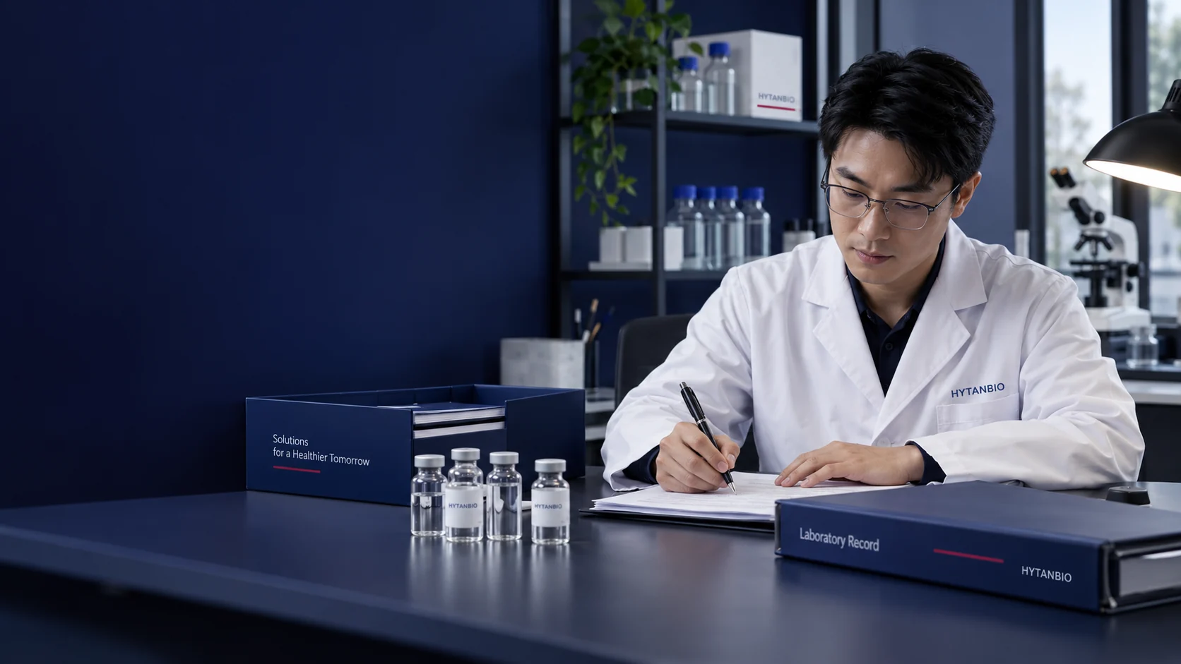 An East Asian male quality coordinator at a documentation desk with upright clear solution vials and a closed laboratory record binder, matte navy document tray and practical side lamp — illustrative development scene