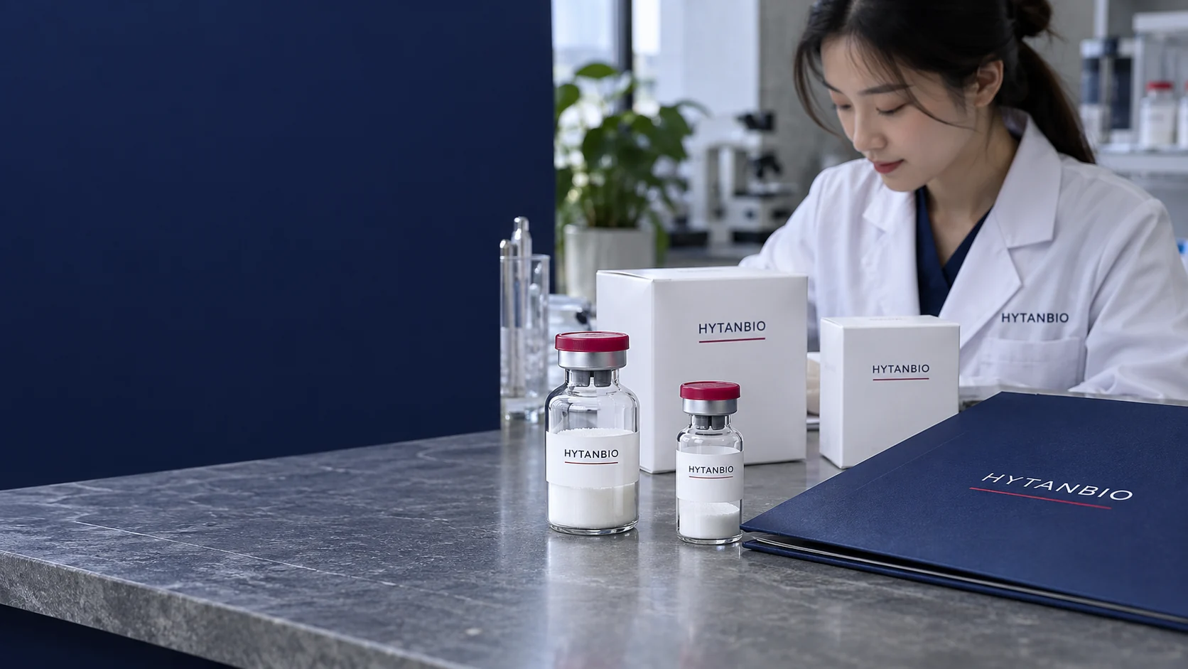 Upright sealed lyophilized sample vials with visible white dry cake in two glass sizes, berry caps, white cartons and a navy product folder on a gray stone formulation counter, quiet natural daylight — illustrative development scene