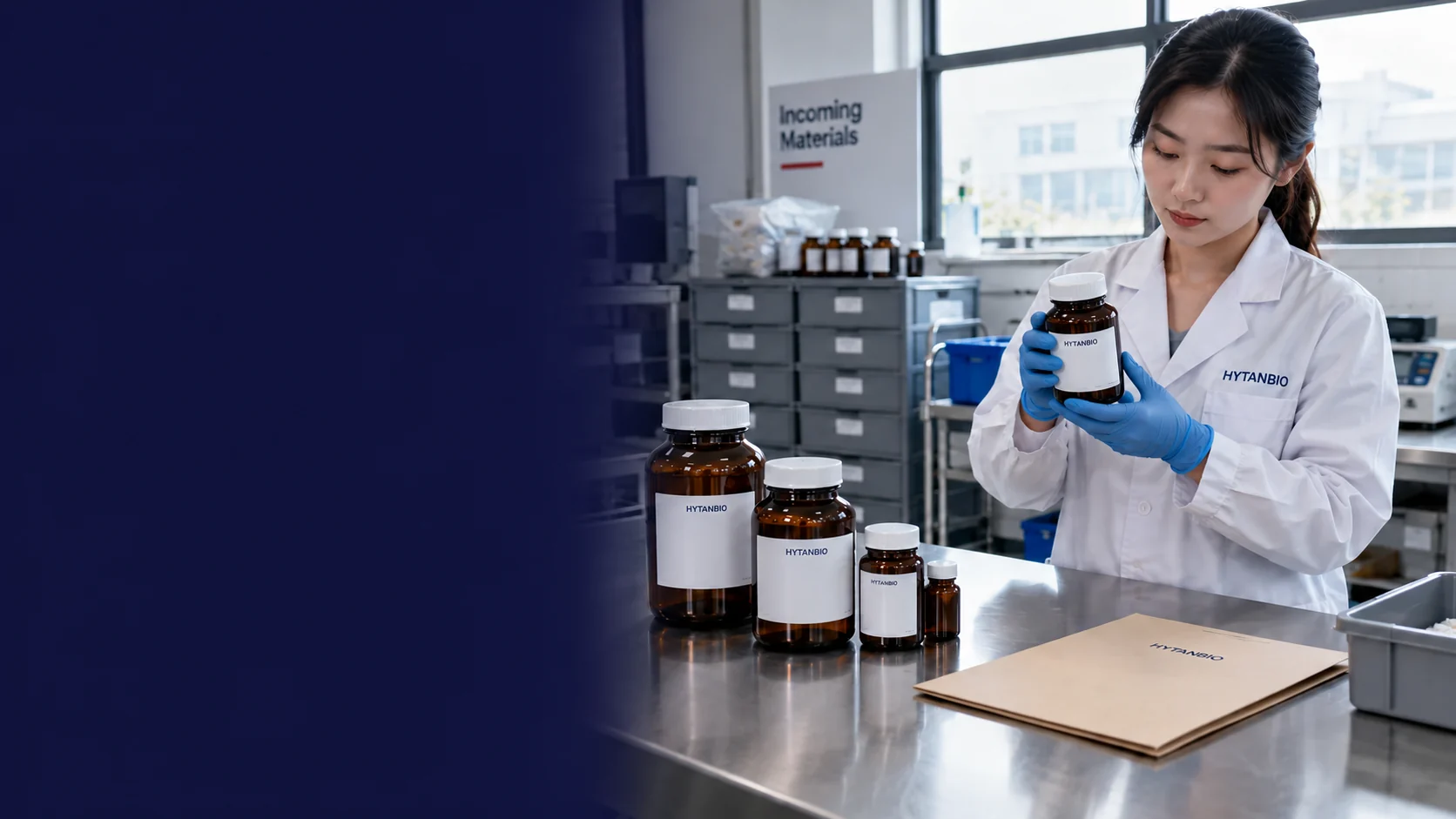 Tall capped amber intermediate jars and a plain receiving folder on a brushed steel incoming-material bench, gray storage drawers and daylight from an industrial window behind — illustrative development scene