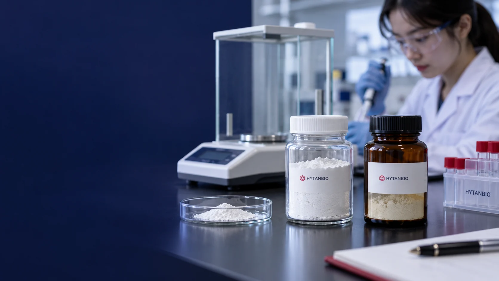Close environmental still life of a clear capped jar of coarse white powder and a sealed amber jar of pale powder, with a dry glass sample dish and laboratory balance behind; unique shallow bench-level angle — illustrative development scene
