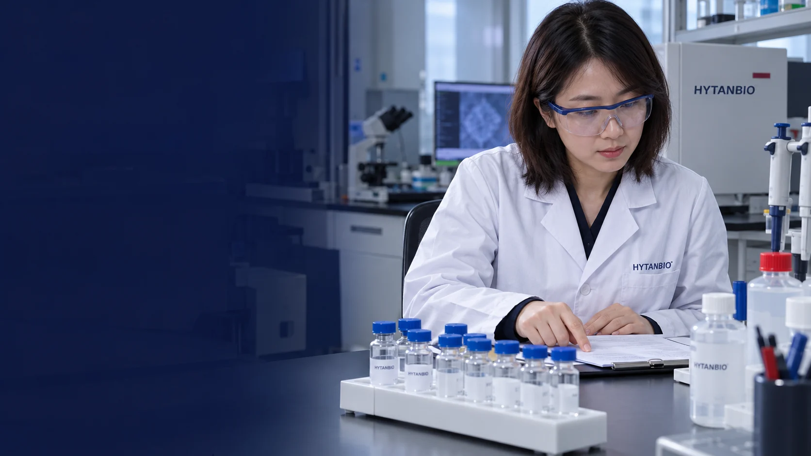 Random East Asian adult female researcher with shoulder-length hair and blue-framed safety glasses inspecting a stationary vial rack; her hands point at a record, never hold a vial — illustrative development scene