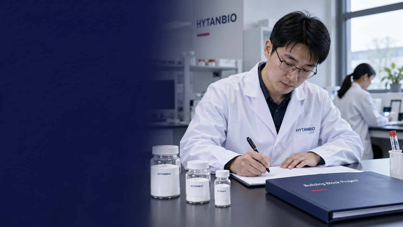 An East Asian male specialist writing a laboratory material brief beside capped powder jars and a closed building-block project folder, upper right side window and understated white-gray interior — illustrative development scene