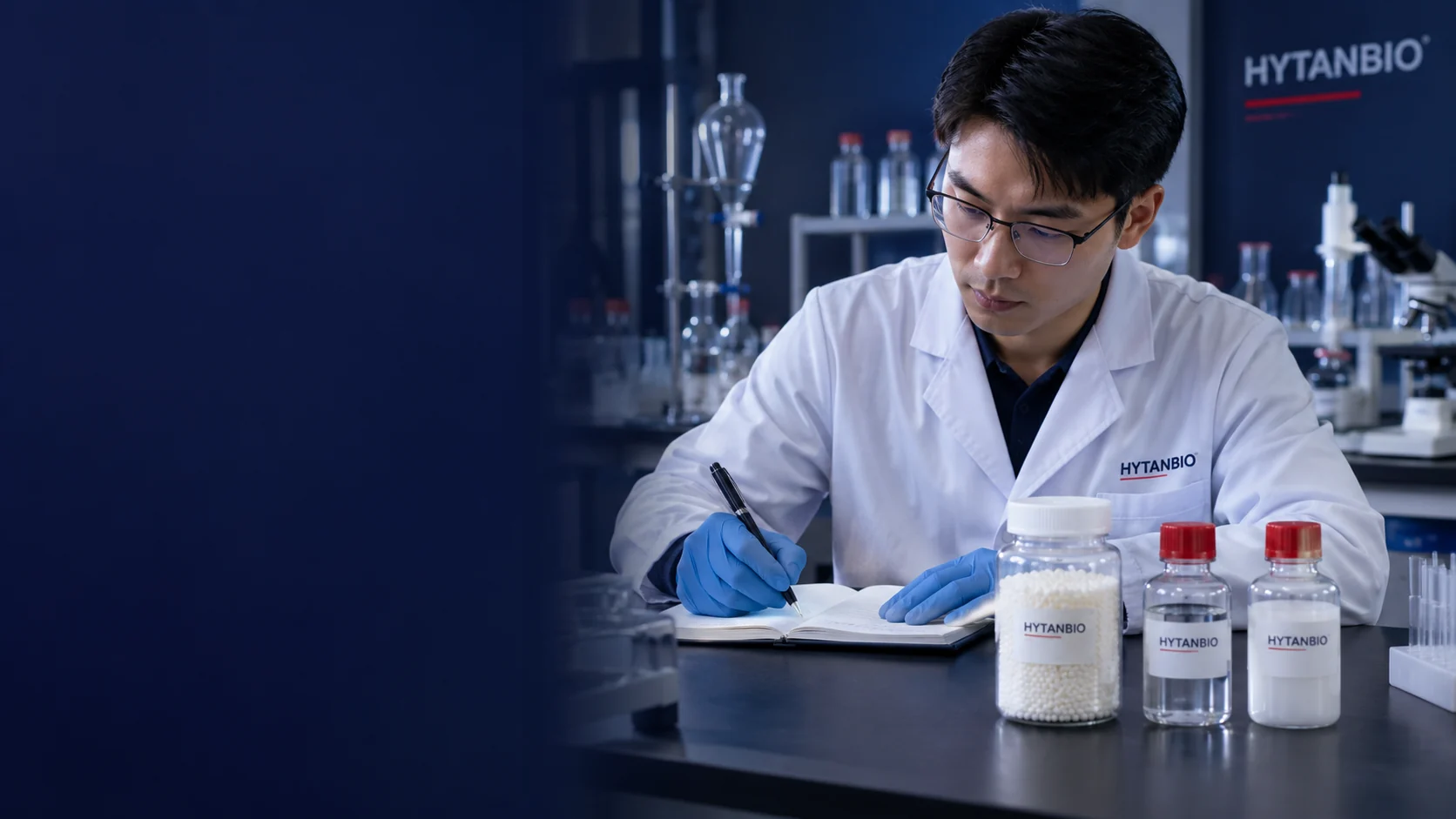 An East Asian male laboratory specialist taking notes beside a straight bead sample jar and two sealed reagent bottles on a dark slate workbench, glass equipment safely parked behind — illustrative development scene