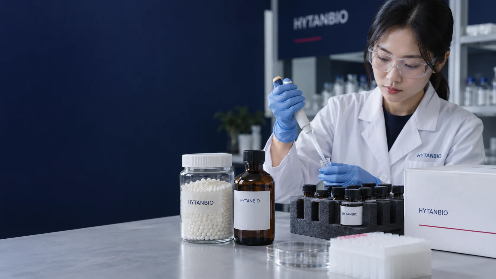 Clear resin-bead jar, closed amber reagent bottle, protective bottle dividers and white sealed supply carton at different depths on a pale industrial countertop with navy backdrop — illustrative development scene