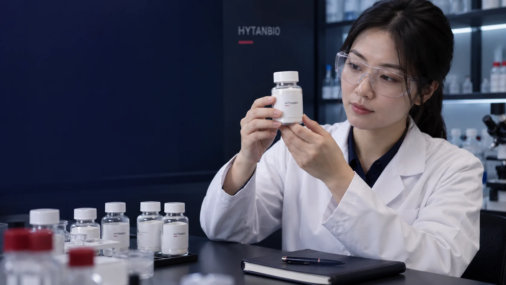 An East Asian procurement scientist inspects a sealed material bottle beside a closed notebook — illustrative development scene