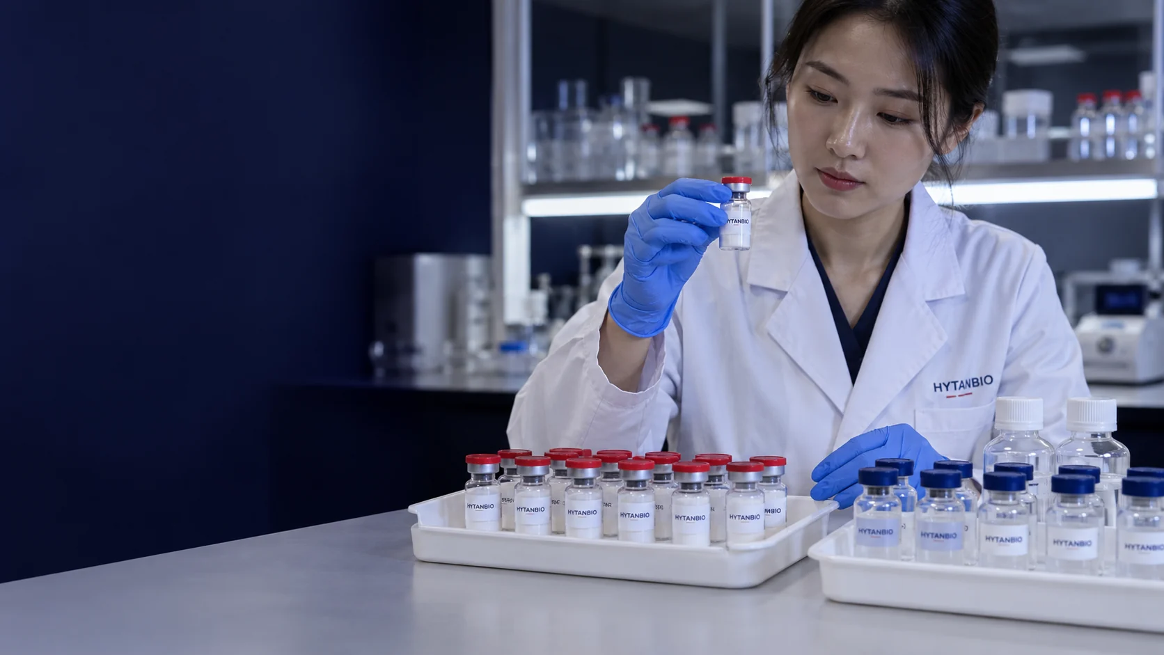 Upright lyophilized sample vials and separate clear laboratory solution containers in two distinct white trays — illustrative development scene