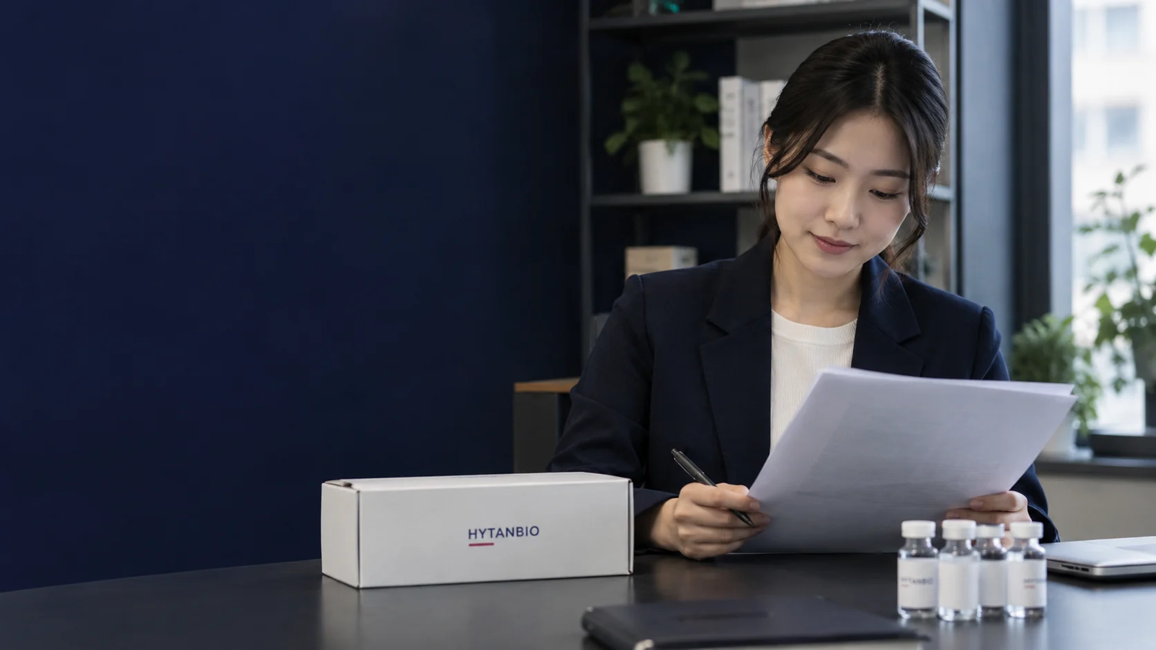 An East Asian project coordinator reviews a neutral requirements sheet beside a closed sample carton — illustrative development scene
