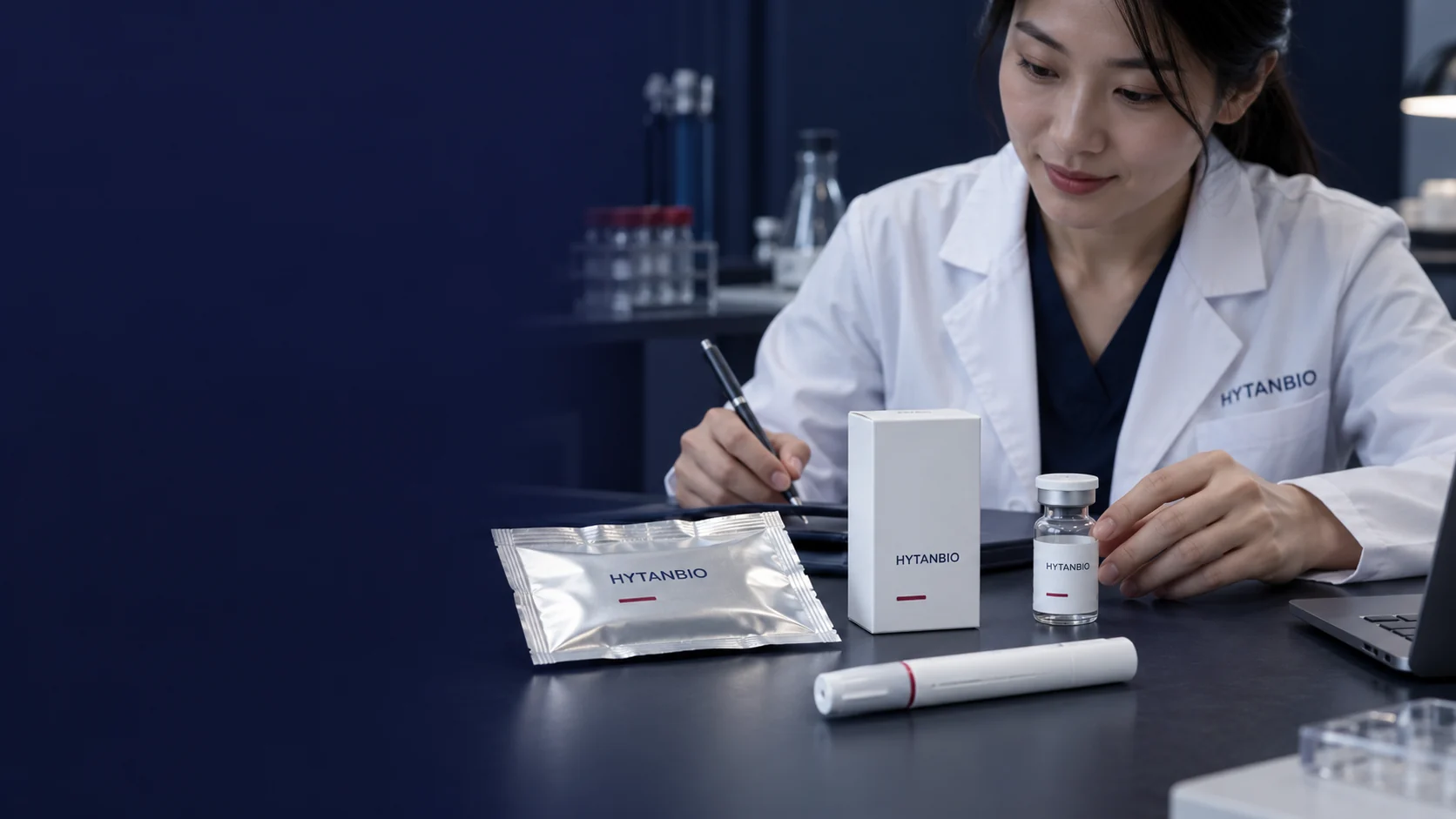 A flat silver sachet, white vial carton and capped empty pen housing laid separately on a technical desk — illustrative development scene
