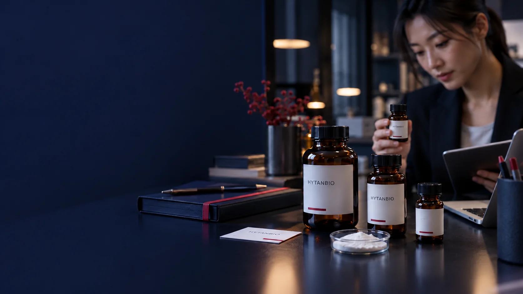 A macro still life of upright amber ingredient containers, a closed reference notebook and a small plain identity card on a dark technical desk — illustrative development scene