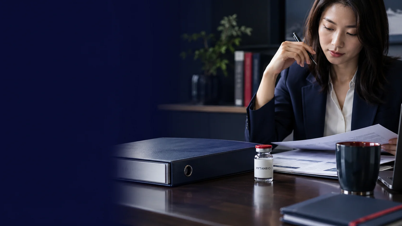 A closed navy binder, unreadable report pages and an upright closed sample vial on a naturally lit review desk — illustrative development scene