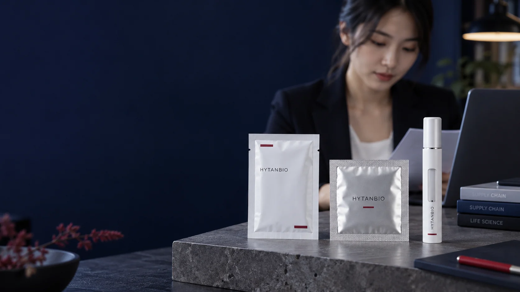 A flat sealed film sachet, square silver patch pouch and empty capped pen-format housing arranged separately on a matte stone sample shelf — illustrative development scene