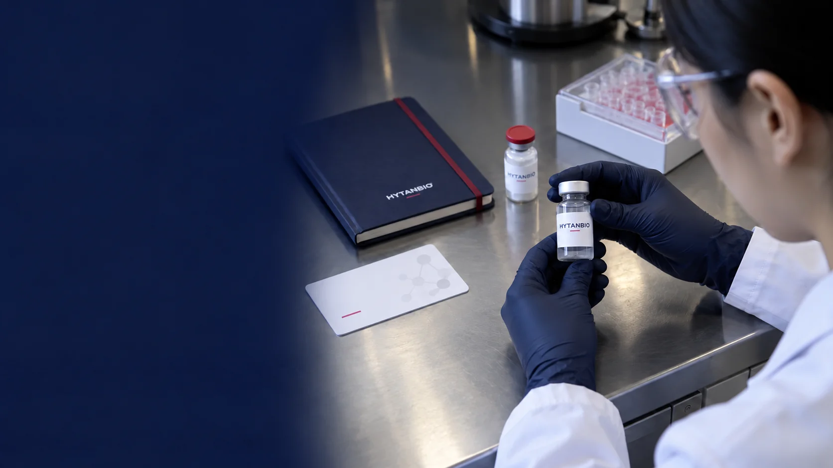 A closed notebook, reference card and two upright small containers on a stainless steel worktop — illustrative development scene