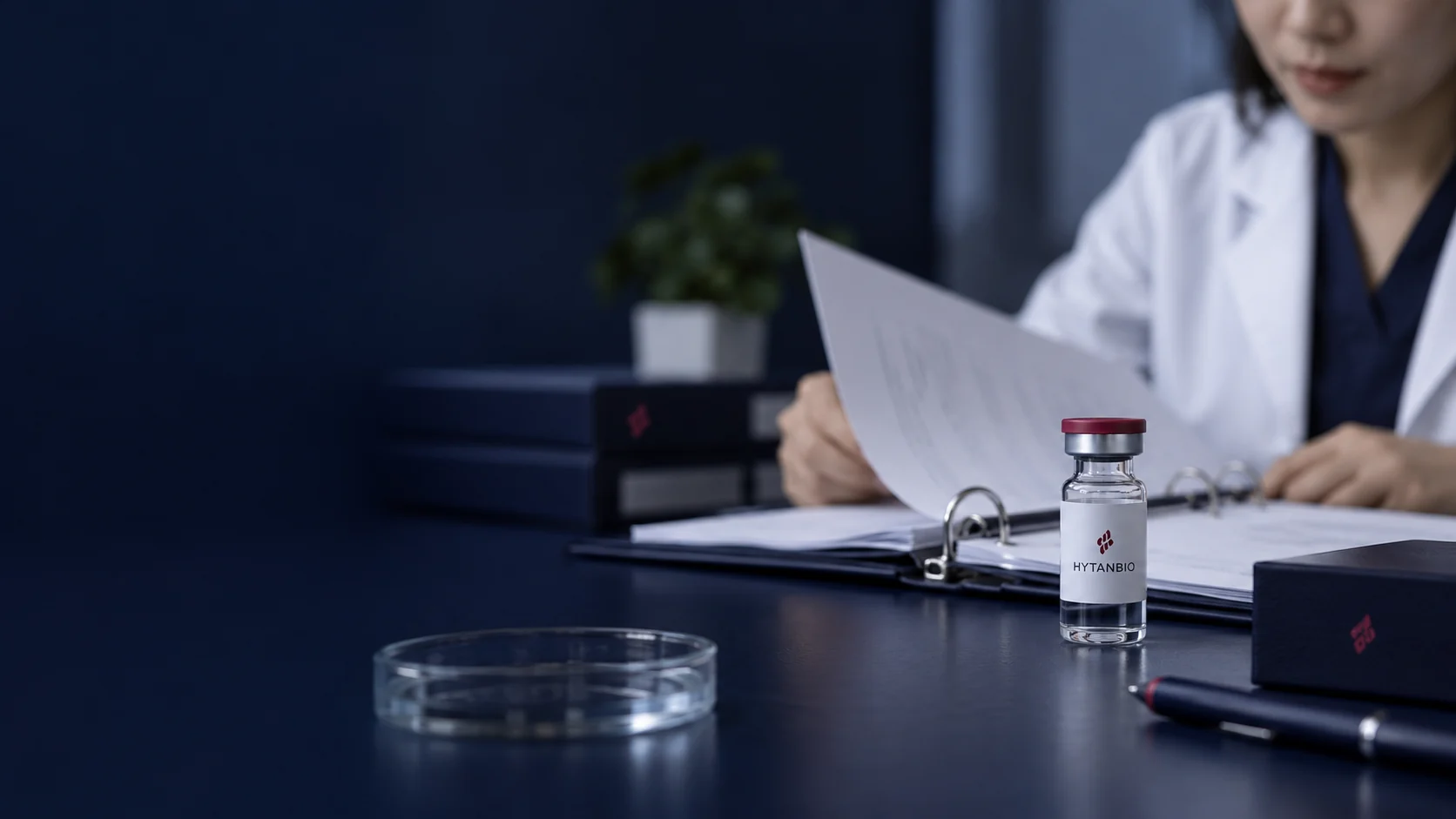 A navy file binder opened to deliberately out-of-focus pages beside a sealed glass sample vial — illustrative development scene