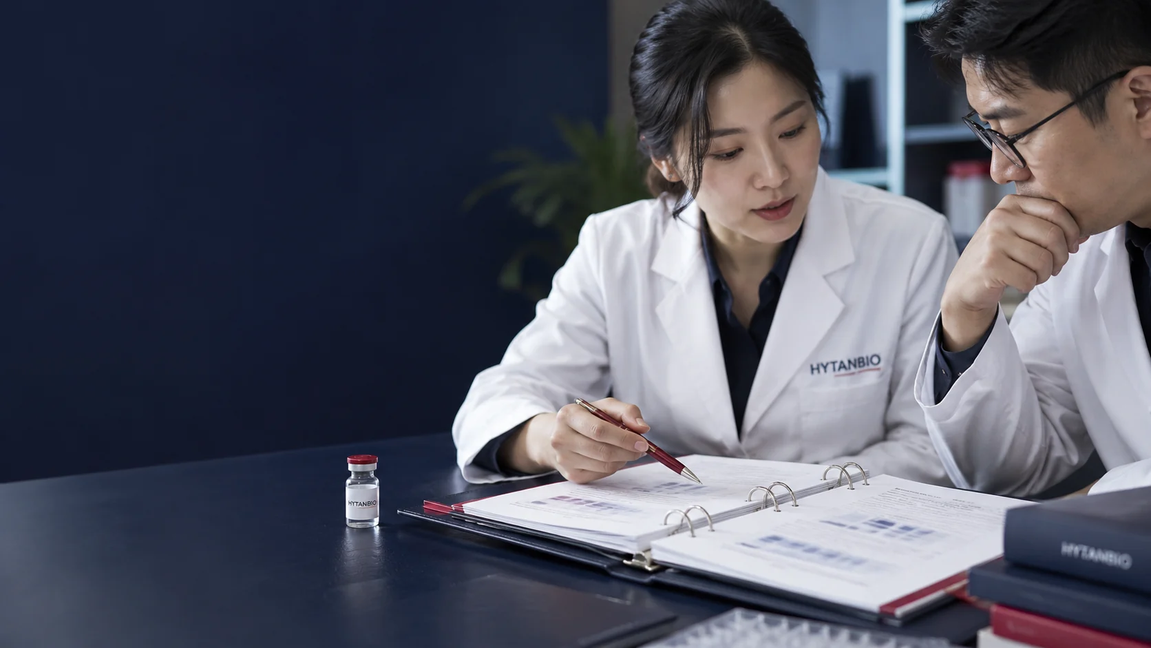 An open review binder with deliberately unreadable report pages and a small capped glass vial — illustrative development scene