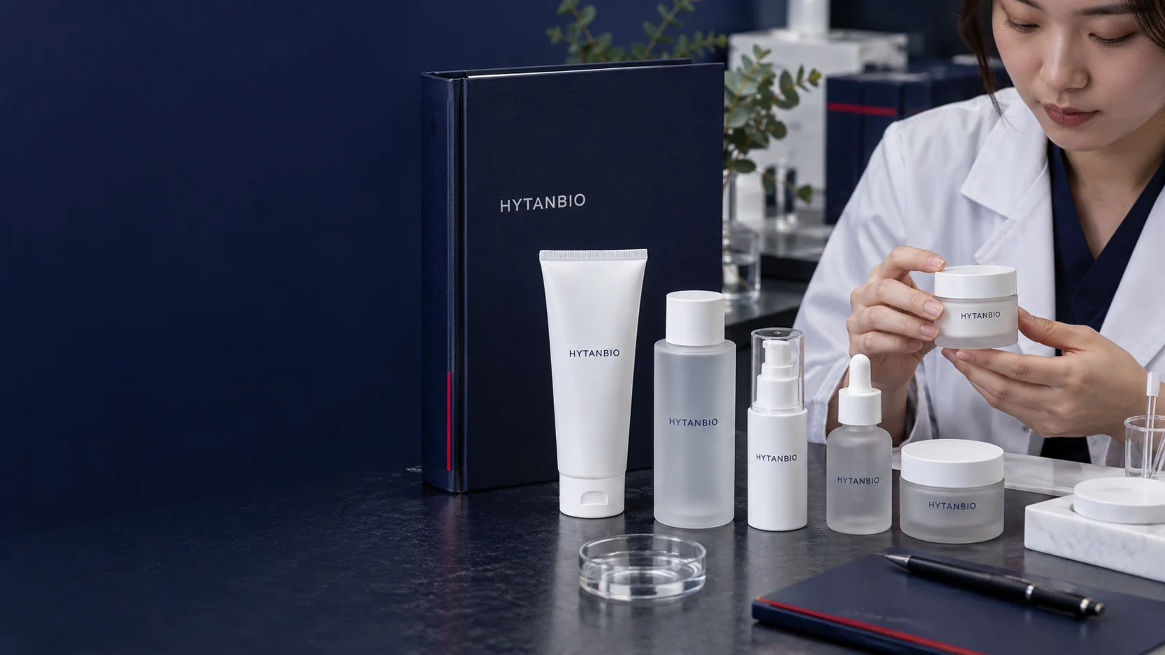 Several neutral cosmetic package prototypes beside a navy specification binder, realistic matte materials — illustrative development scene